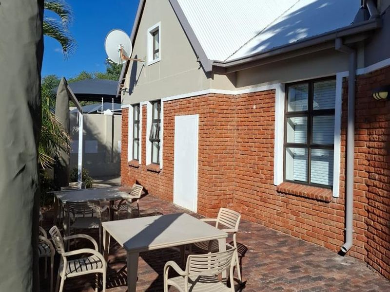 A paved outdoor patio area featuring an exposed brick facade, corrugated metal roofing, and functional downpipe infrastructure.