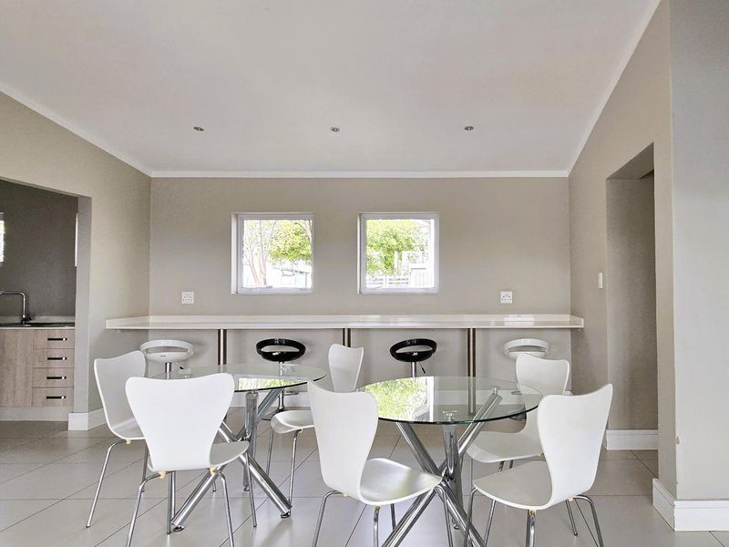 An open-plan living and kitchen area featuring tiled flooring, recessed lighting, and a built-in breakfast bar with integrated kitchen cabinetry and sink.