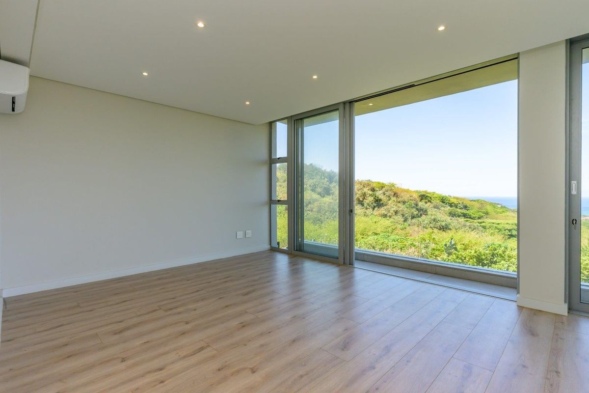 A bright, empty bedroom featuring modern laminate flooring, recessed lighting, a split-system air conditioner, and large sliding glass doors with scenic coastal views.