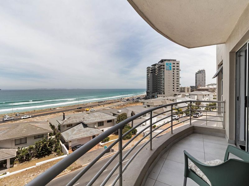 A spacious balcony featuring tiled flooring and a metal railing, offering expansive coastal and urban views.