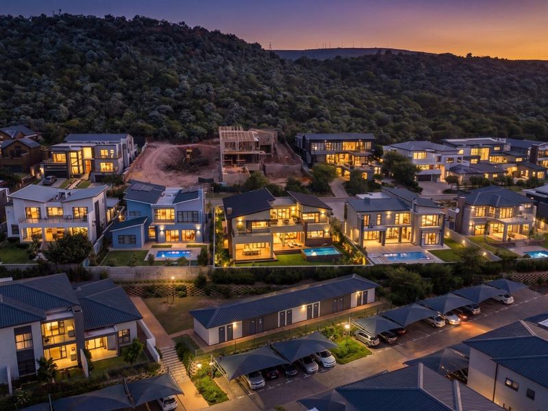 Aerial view of a modern residential estate at dusk, featuring multiple luxury homes with swimming pools, landscaped gardens, and covered parking facilities.