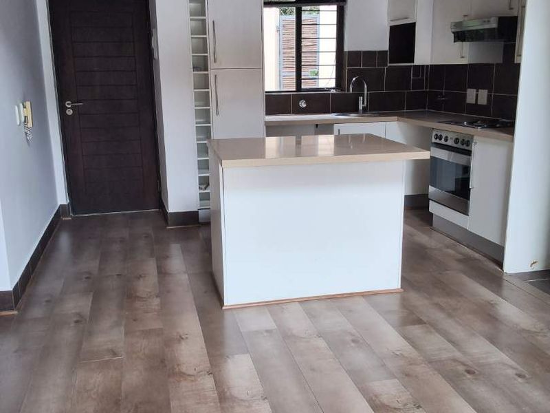 Modern kitchen featuring an island, built-in oven, hob, extractor fan, and stylish laminate flooring under exposed timber ceiling beams.