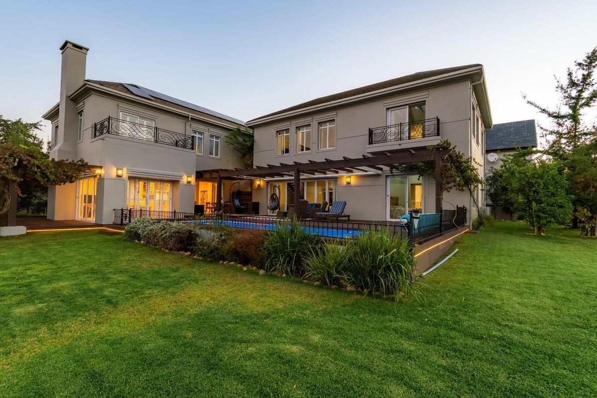 Rear view of a two-story house featuring a swimming pool, timber pergola, landscaped garden, and upper-level balconies with decorative wrought iron railings.