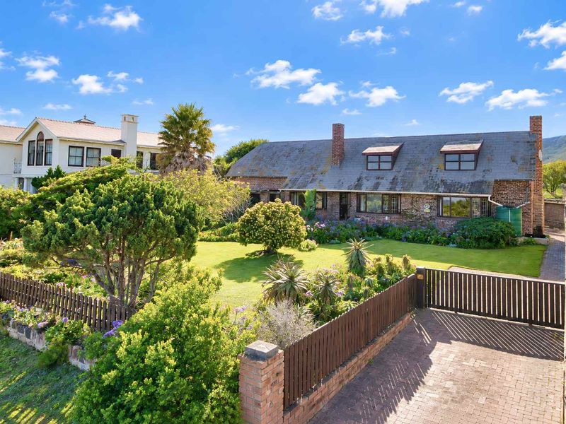 A charming brick-faced home featuring a slate roof, dormer windows, and a well-maintained garden with a paved driveway and timber fencing.
