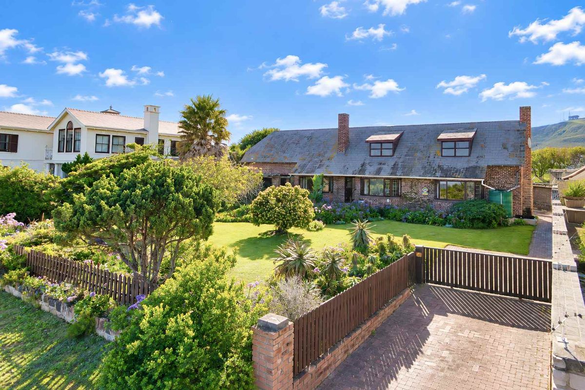 A charming brick-faced home featuring a slate roof, dormer windows, and a well-maintained garden with a paved driveway and timber fencing.