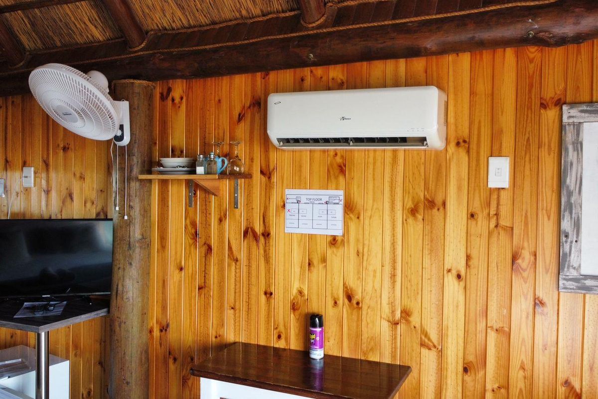A rustic interior space featuring timber-clad walls, a thatched roof structure, and a wall-mounted air conditioning unit.