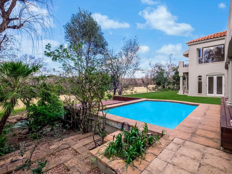 Outdoor pool area featuring a swimming pool, tiled decking, timber accents, and landscaped garden with views of the surrounding estate.