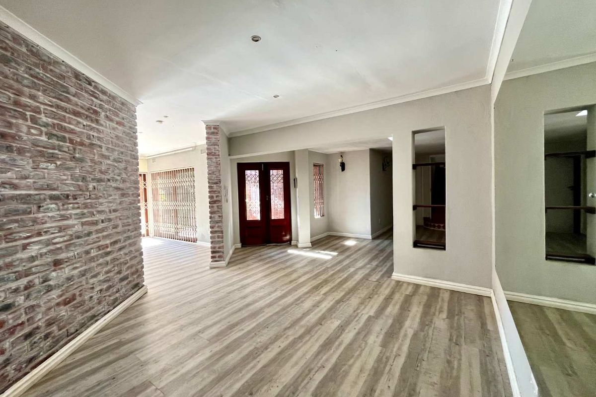 Spacious open-plan living area featuring modern laminate flooring, an exposed brick feature wall, and neutral tones, providing a versatile blank canvas for interior design.