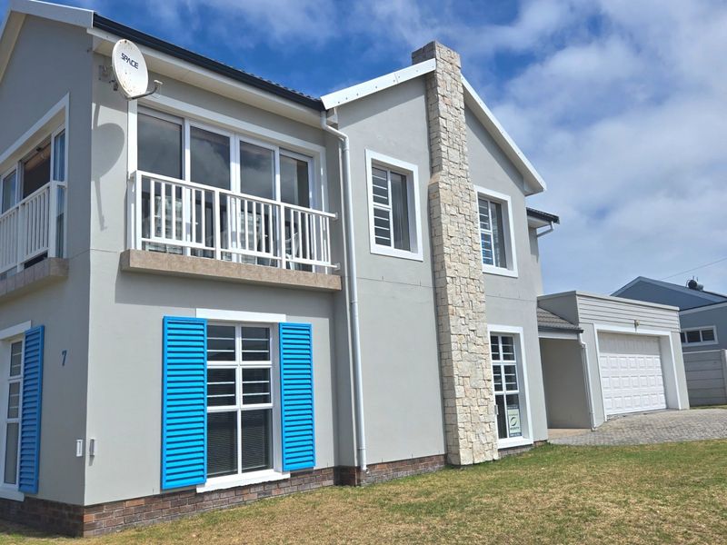 A well-maintained two-story house featuring a stone-clad chimney, a balcony, blue window shutters, and an attached garage with a paved driveway.