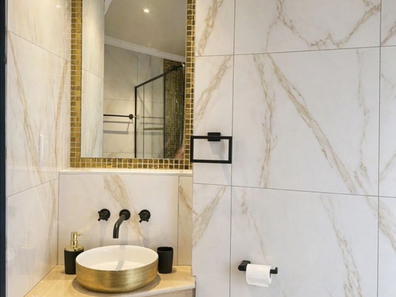 Modern bathroom featuring marble-look wall tiles, a gold-accented basin, and sleek black matte fixtures for a contemporary aesthetic.