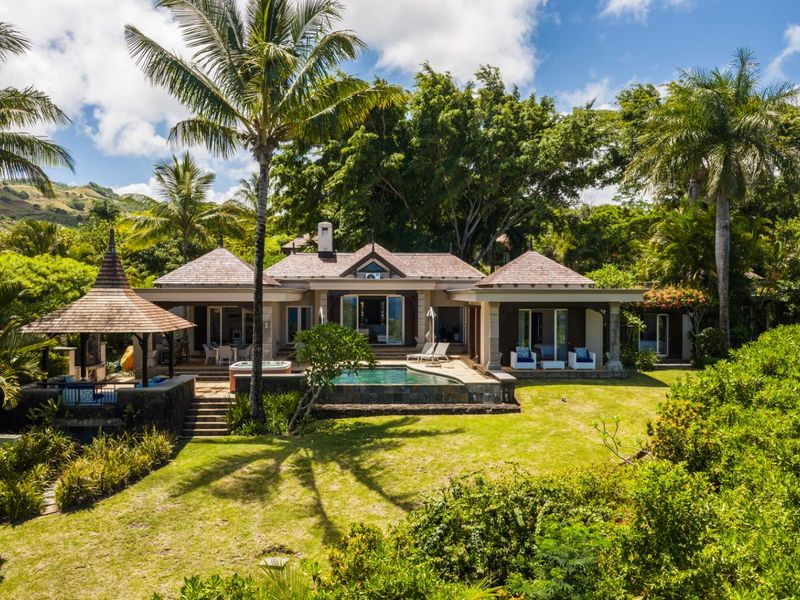 A beautiful rear exterior view of a luxury residence featuring a private swimming pool, covered patio, and a detached gazebo set in lush gardens.