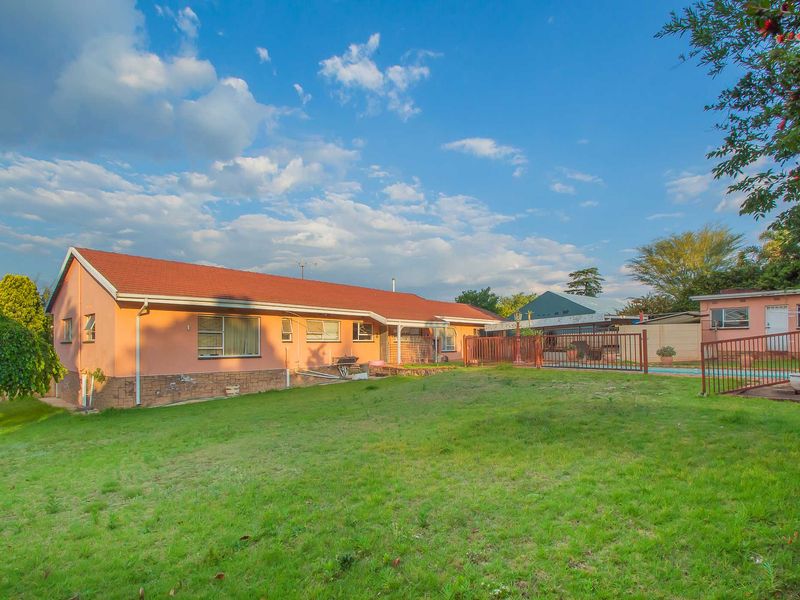 Rear view of the house featuring a spacious lawn, swimming pool area, and traditional tiled roof architecture.