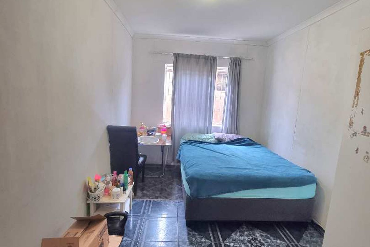 A bedroom featuring dark patterned floor tiles, a central ceiling light, and a window with curtains.