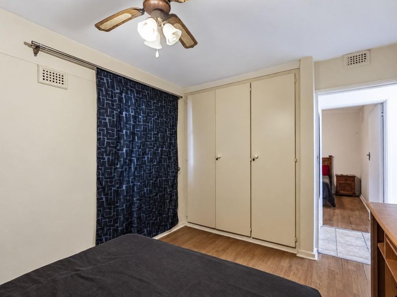 A bedroom featuring a built-in wardrobe, ceiling fan, and ventilation grille, with a doorway leading to an adjacent room.