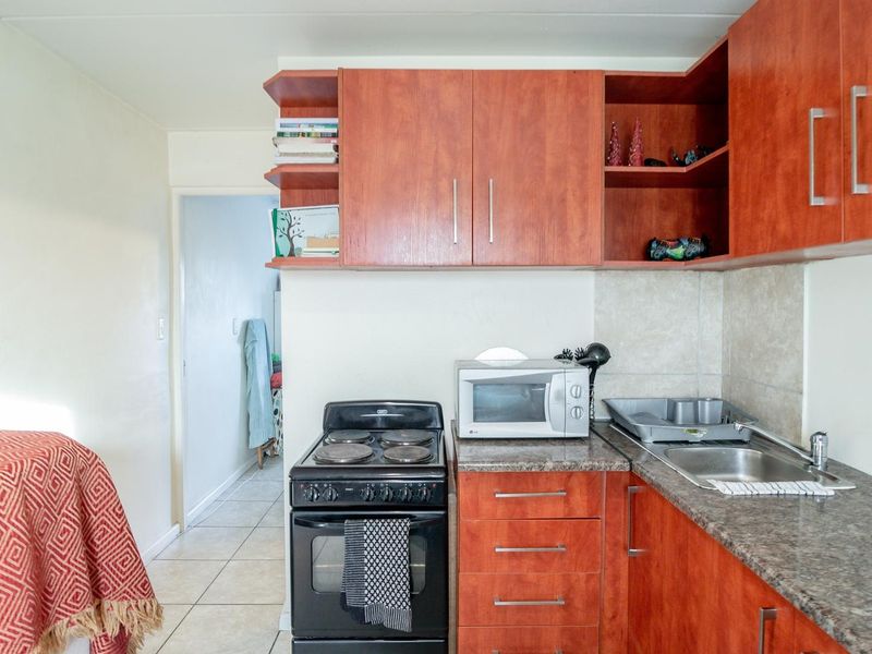 Compact kitchen featuring wood-finish cabinetry, stone-look countertops, a stainless steel sink, and a freestanding electric stove with tiled backsplash.
