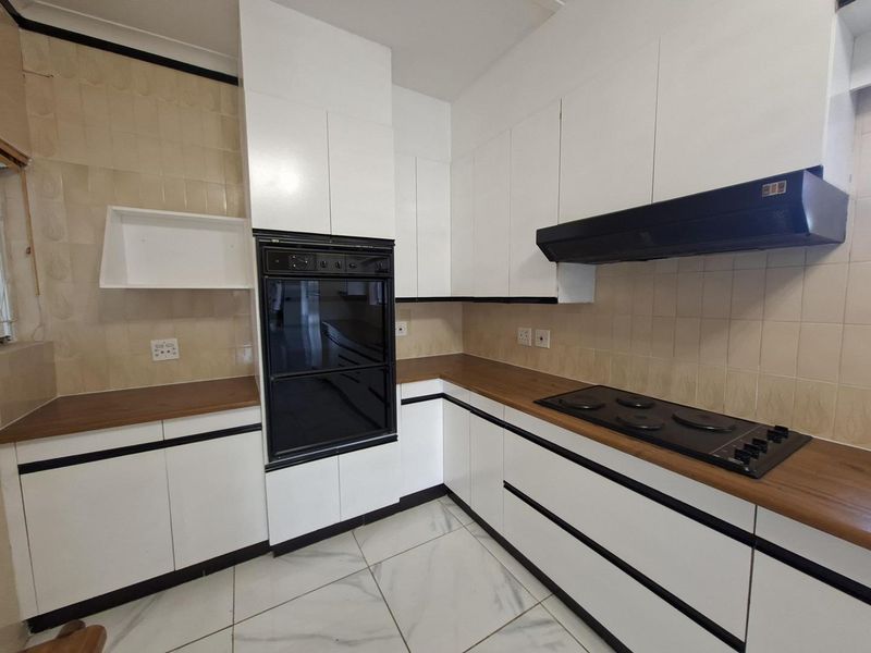 A functional kitchen featuring white cabinetry, wood-look countertops, a built-in oven, and an electric hob with an overhead extractor fan.
