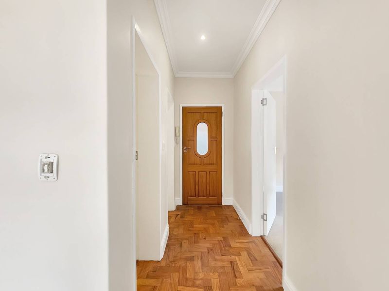 A bright and well-maintained hallway featuring classic parquet flooring, crisp white walls, and elegant coving, leading to multiple rooms.