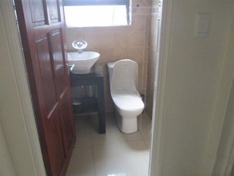 A compact bathroom featuring a modern vessel sink on a vanity cabinet, a toilet, and neutral wall and floor tiling.