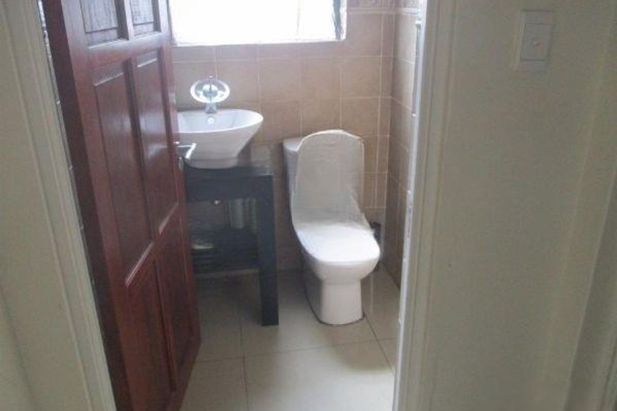 A compact bathroom featuring a modern vessel sink on a vanity cabinet, a toilet, and neutral wall and floor tiling.