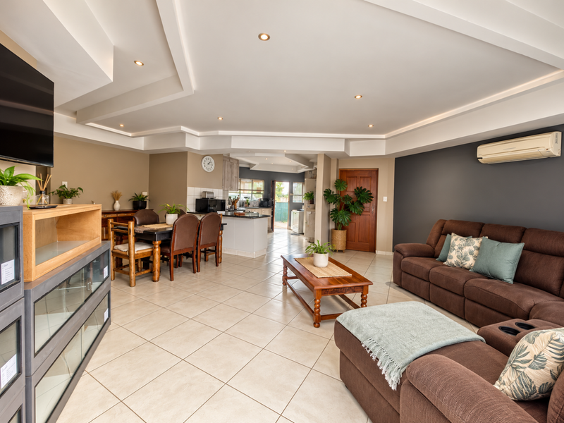 Spacious open-plan living and dining area featuring tiled floors, recessed ceiling lighting, and a modern kitchen with island, seamlessly flowing into the home.
