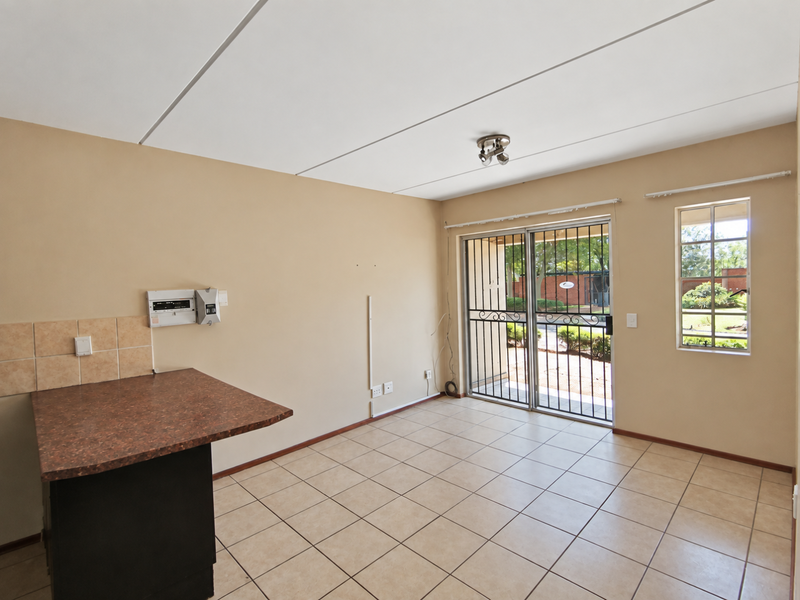 An open-plan living area featuring tiled flooring, a kitchen counter, and a sliding door with a security gate leading to the exterior.