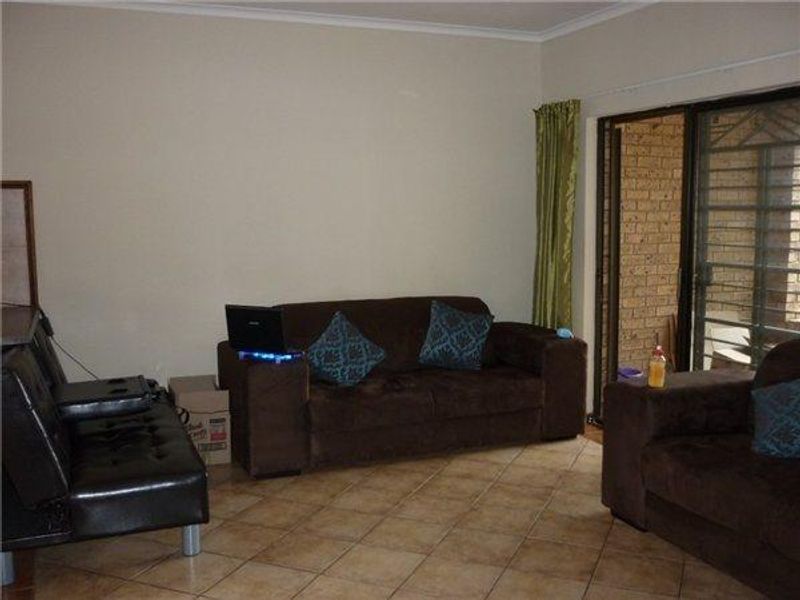 A living room featuring tiled flooring and a sliding glass door with an integrated security gate, providing access to an outdoor area.
