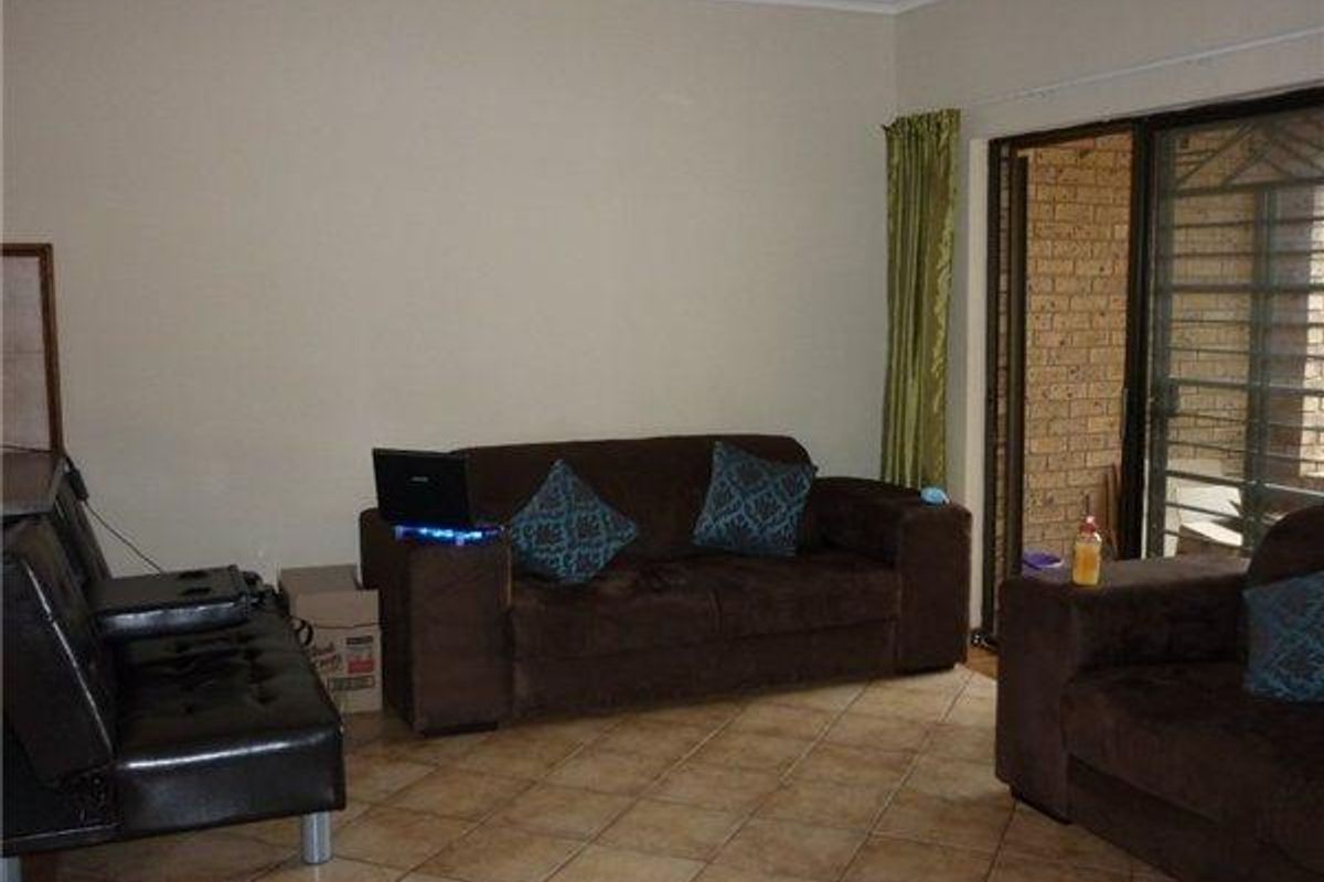 A living room featuring tiled flooring and a sliding glass door with an integrated security gate, providing access to an outdoor area.