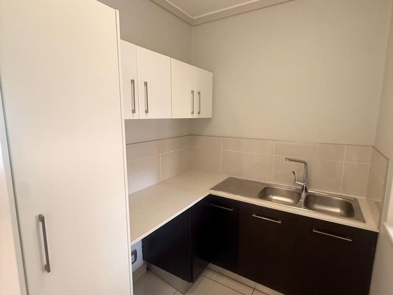A clean and functional laundry area featuring built-in dark lower cabinetry, white upper cabinets, a stainless steel double sink, and neutral tiled flooring.