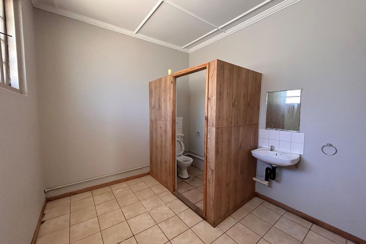 A functional bathroom space featuring a wall-mounted basin and a partitioned toilet area with tiled flooring and neutral wall finishes.