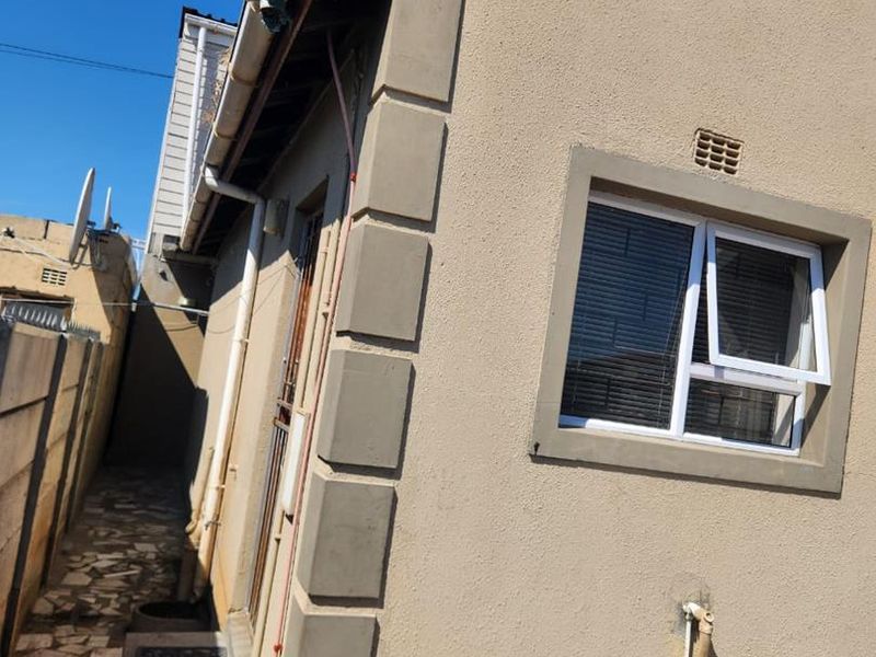 Side view of the property showing the exterior wall, casement window, and paved side walkway with exposed roof eaves.