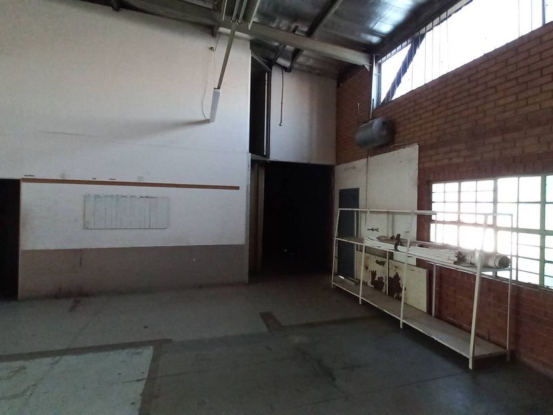 Spacious industrial warehouse interior featuring exposed brickwork, high ceilings with metal trusses, large grid windows, and built-in metal storage shelving.
