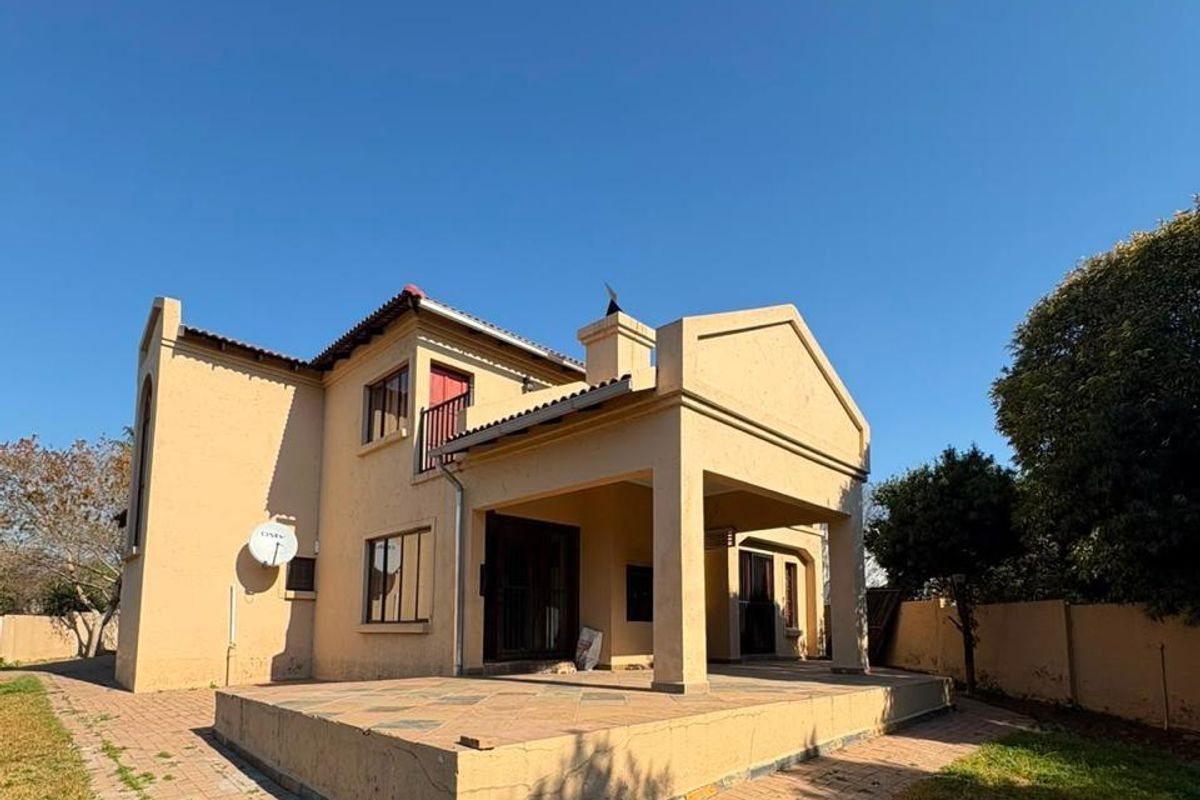 Rear view of the house featuring a covered patio area, a small upper-level balcony, and paved outdoor pathways.