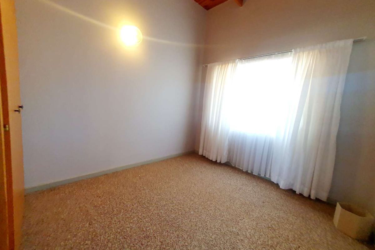 A vacant bedroom featuring high vaulted timber ceilings, carpeted flooring, and a large window with natural light.