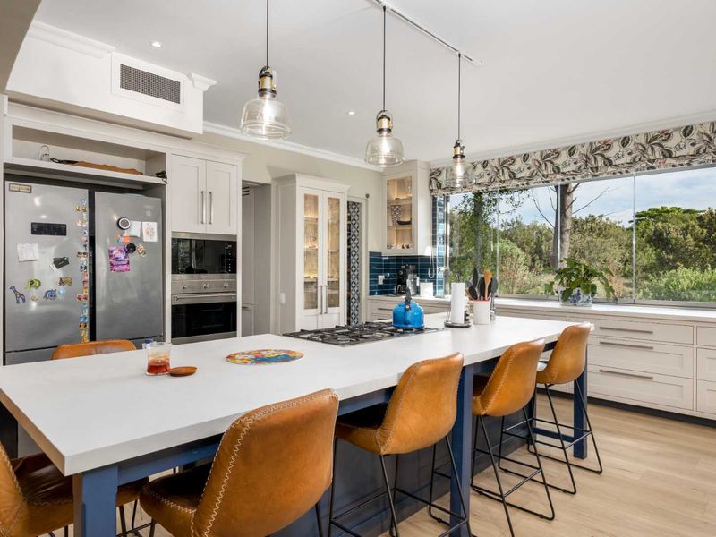 Modern kitchen featuring a large central island with gas cooktop, built-in appliances, ample cabinetry, and large windows overlooking the garden.