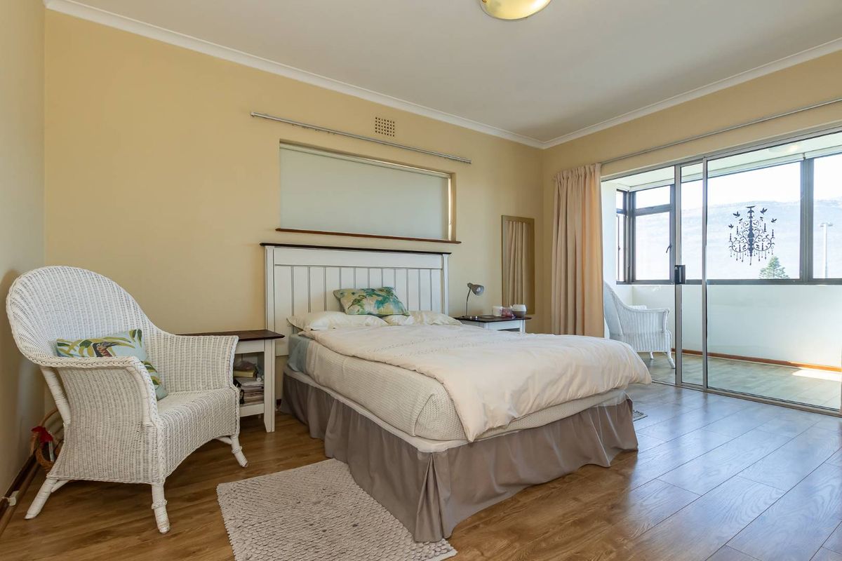 A well-lit bedroom featuring laminate flooring, neutral walls, and sliding glass doors that open onto a private balcony.