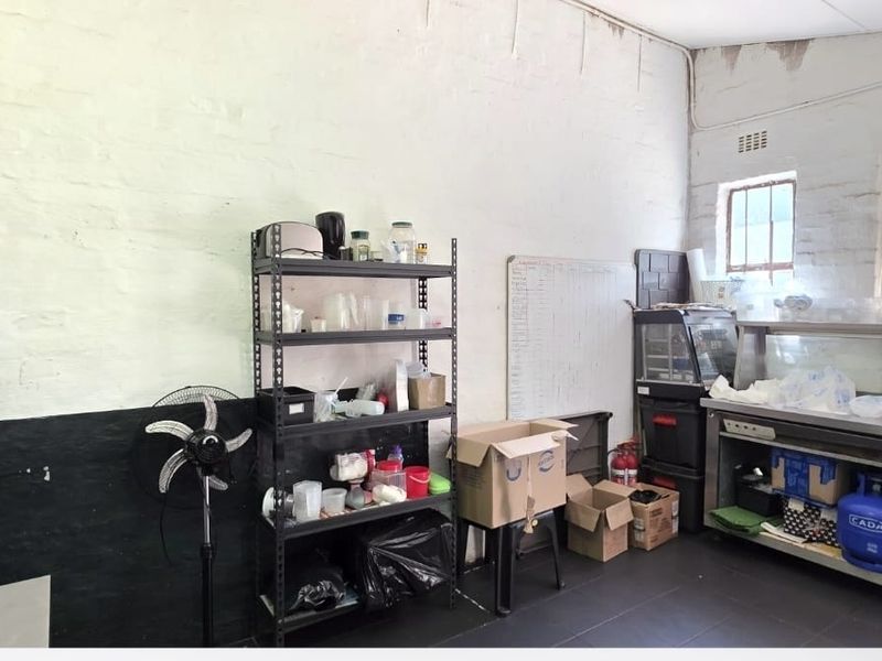 A functional commercial kitchen area featuring stainless steel prep surfaces, tiled flooring, and exposed brick walls, requiring cosmetic updates.