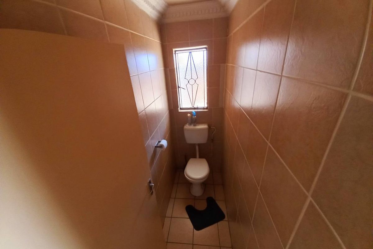 A compact guest toilet featuring floor-to-ceiling ceramic wall tiles, tiled flooring, and a small window for natural light.