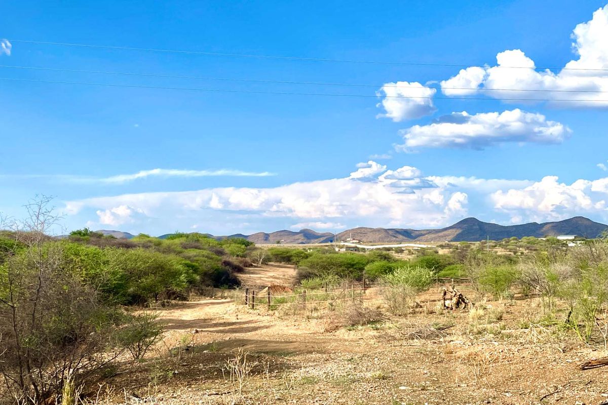A wide-angle view of the vacant commercial land featuring natural vegetation, a dirt access track, and wire fencing against a mountain backdrop.