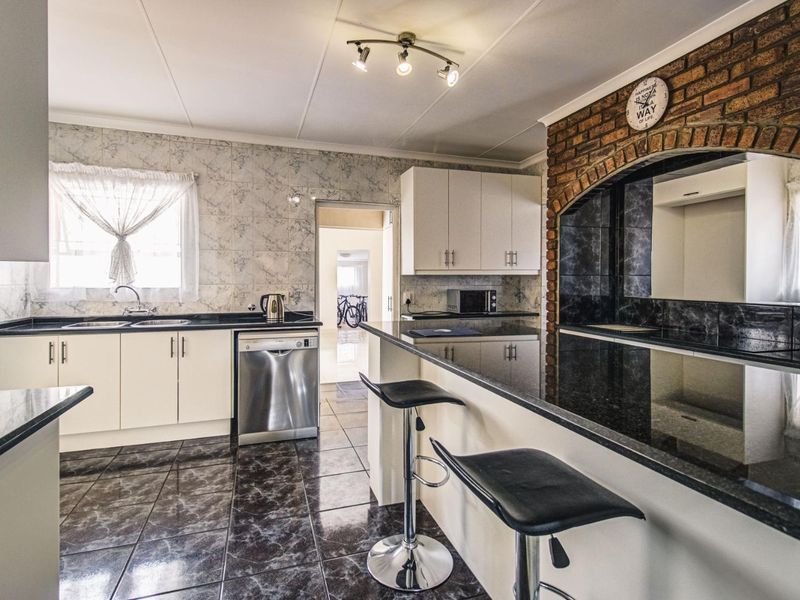 A functional kitchen featuring white cabinetry, dark granite countertops, a breakfast bar, and a distinctive exposed brick feature wall with tiled flooring.