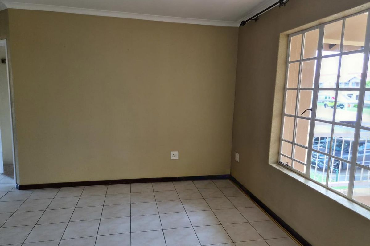 A vacant bedroom featuring neutral wall paint, tiled flooring, and a large window with security bars.