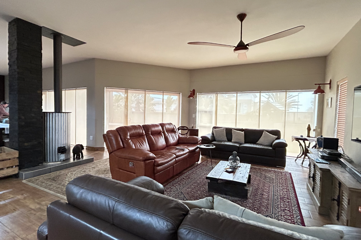 Spacious living area featuring a prominent stone-clad fireplace, large windows with roller blinds, and a modern ceiling fan.