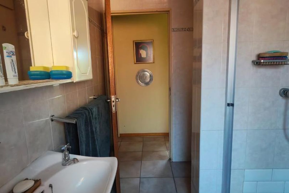 A functional bathroom featuring a pedestal basin, a shower enclosure with a pebble-style floor, and tiled walls.