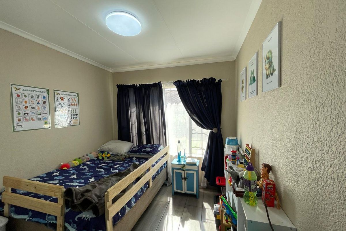 A functional bedroom featuring tiled flooring, neutral wall finishes, and a window with curtain treatments, providing a comfortable space for a child.