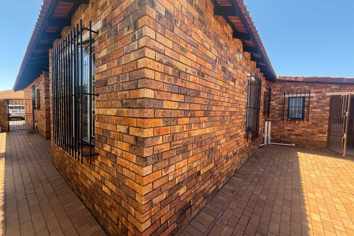 A view of the rear exterior of the townhouse featuring face brick walls, security bars on windows, and a paved courtyard area.