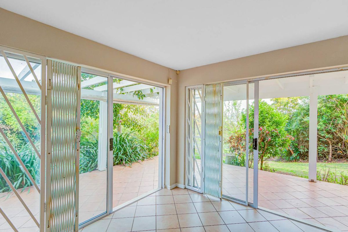 Bright sunroom featuring tiled flooring and dual sliding glass doors opening onto a covered patio and lush garden area.