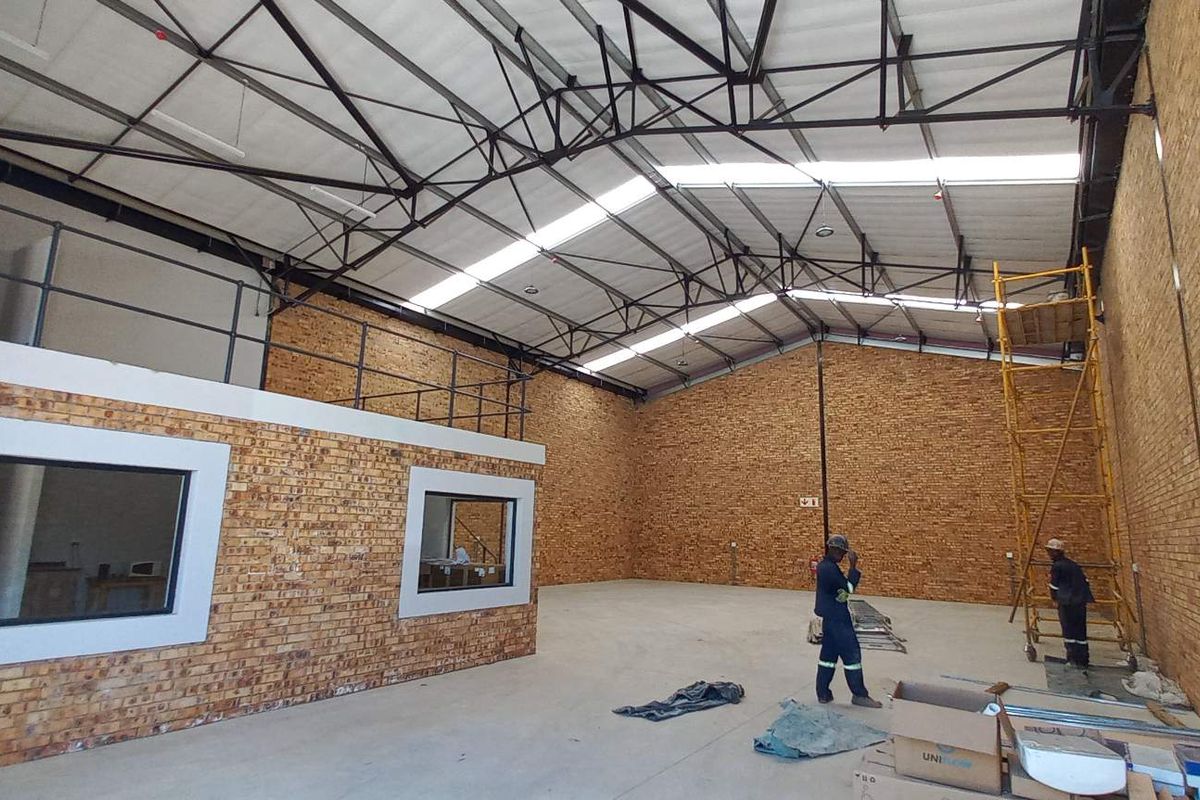 Spacious industrial warehouse unit featuring high ceilings with exposed steel trusses, facebrick walls, concrete flooring, and a mezzanine level for additional storage or office space.