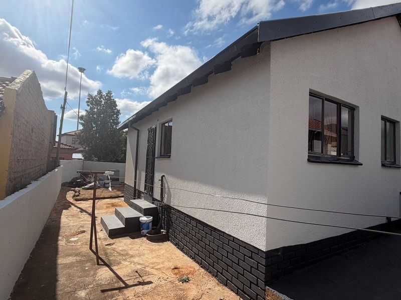 Rear view of the property featuring a clean plastered facade, dark brick base, and aluminium window frames with a concrete pathway.