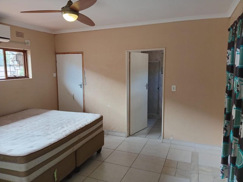 A bedroom featuring tiled flooring, a ceiling fan, and an air conditioning unit, with an adjoining en-suite bathroom.