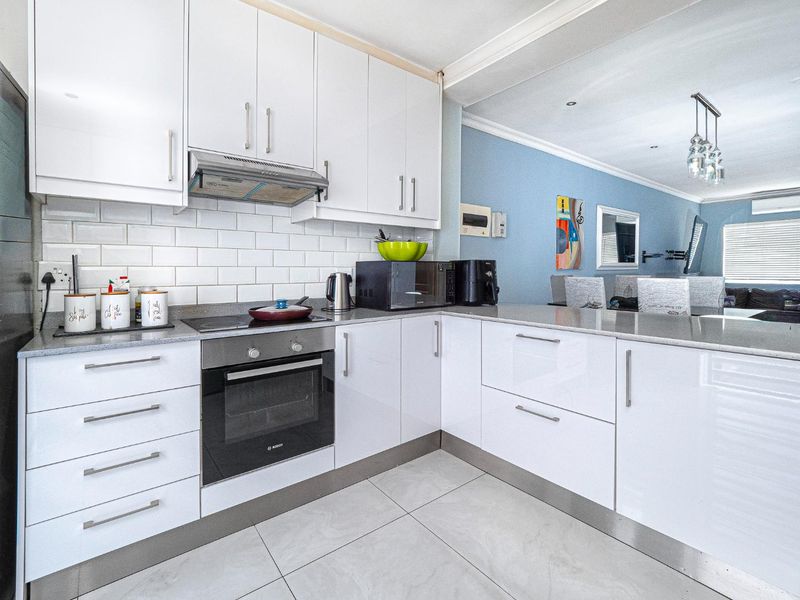 Modern open-plan kitchen featuring white gloss cabinetry, stone countertops, subway tile backsplash, and integrated appliances, flowing into the adjacent living area.