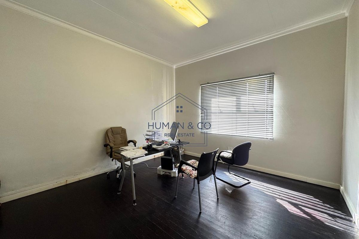 A functional office space featuring dark wood flooring, venetian blinds, and a central fluorescent light fixture.